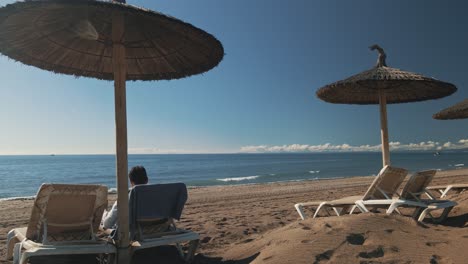 Mann-Entspannt-Sich-An-Einem-Sonnigen-Strand-Mit-Sonnenschirm-Und-Stühlen