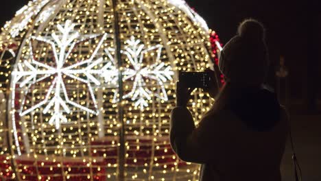 Woman-Taking-Pictures-with-a-Phone-of-a-Christmas-Lights-at-Night