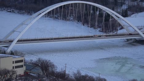 1-2-Winter-forest-evening-zoom-panout-modern-architectural-white-led-tied-arch-bridge-over-icy-reflective-river-melting-with-many-white-cars-trucks-crossing-and-moving-cube-van-in-super-SLOW-MOTION