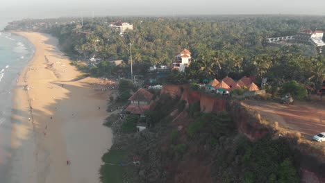Varkala-Cliff-with-a-sight-of-the-sea-and-the-lush-vegetation-near-the-shoreline,-in-India---Aerial-Panoramic-shot