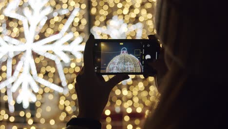 Woman-Taking-Pictures-with-a-Phone-of-a-Christmas-Decoration-at-Night