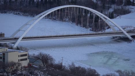 2-2-Winter-forest-evening-zoom-panout-modern-architectural-white-tied-arch-bridge-over-icy-reflective-river-melting-with-many-white-cars-trucks-crossing-moving-cube-van-one-way-in-super-SLOW-MOTION