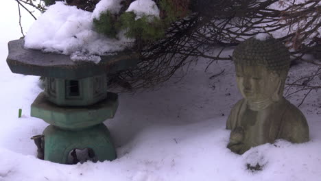 Snow-slowly-melts-and-drips,-piled-atop-a-Japanese-lantern,-and-Buddha-statue