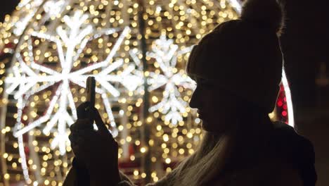 Woman-Taking-Pictures-with-a-Phone-of-a-Christmas-Lights-at-Night
