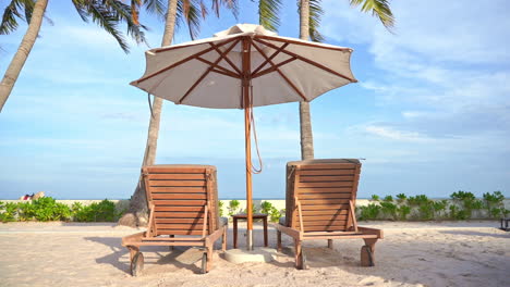 Zwei-Leere-Holzsitze-Und-Ein-Sonnenschirm-Unter-Palmen-In-Einem-Tropischen-Reiseziel-Mit-Meerblick-Und-Weißem-Sandstrand