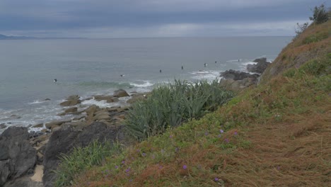 Surfers-relaxing-by-the-rocky-shoreline-of-Lennox-Point,-Australia--slow-pan