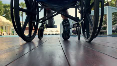 Person-in-a-wheelchair-sitting-on-a-deck-or-patio-overlooking-the-swimming-pool---low-angle-view-of-wheelchair-and-feet