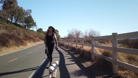 Hispanic-female-walking-white-Maltese-dog-on-bike-path-during-a-clear-day
