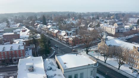Winter-establishing-shot-of-snow-covered-homes-and-businesses-in-small-town-square-as-traffic-passes-by