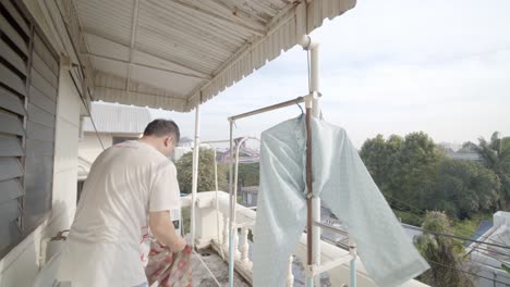 Asian-man-on-his-apartment-balcony-hanging-up-freshly-washed-clothes-to-dry---slow-motion
