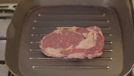 Rare-ribeye-steak-being-placed-in-grill-pan