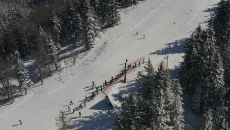 Skiers-gather-at-a-track-in-Kope-resort-Slovenia-in-the-Pohorje-mountains,-Aerial-tilt-up-shot