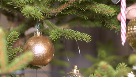 Primer-Plano-De-La-Mano-Colgando-Decoración-Brillante-Bola-En-El-árbol-De-Navidad