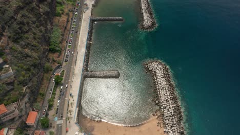Artificial-beach-on-shore-of-Madeira-with-steep-volcanic-cliffs,-aerial