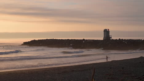 Silhouette-Of-Foghorn-And-A-Person-Watching-Waves-At-The-Beach-In-Bandon,-Oregon-At-Sunset---wide-shot