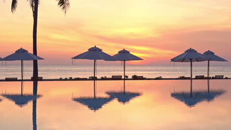 A-dramatic-view-from-a-resort-pool-of-a-sunset-of-pink,-yellow,-and-orange-hangs-over-the-ocean-horizon
