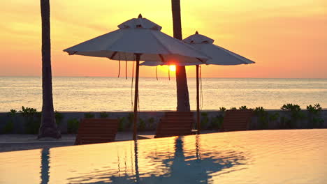 Erstaunliche-Aufnahme-Des-Resorts-Mit-Meerblick-Mit-Infinity-Pool-Und-Sonnenschirmen-Bei-Sonnenuntergang