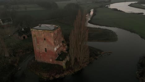 Slow-aerial-descend-showing-the-remains-of-Nijenbeek-castle-revealing-the-early-morning-winter-sunrise-with-ruins-and-tall-tree-in-river-delta-landscape