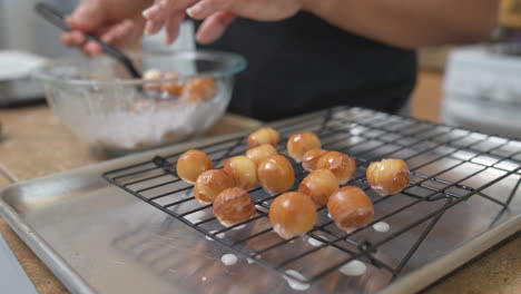 Woman-covers-fresh-donut-holes-in-icing-glaze-and-puts-on-cooling-rack,-Slowmo