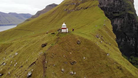 4k-Aerial-beautiful-parallax-of-famous-lighthouse,-Kalsoy-in-the-landscape-Kallur-at-the-Faroe-Islands-with-seagulls-flying-about-on-a-cloudy-day