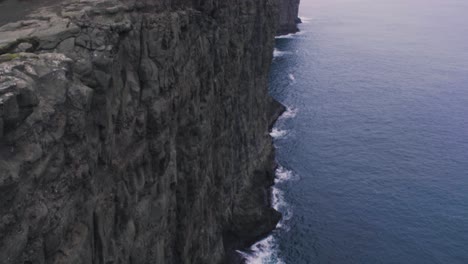 Reveal-tilt-up-of-incredible-and-spectacular-huge-cliff-drop-landscape-with-waves-from-the-northern-atlantic-ocean-crashing-against-the-rocks-on-the-Faroe-Islands