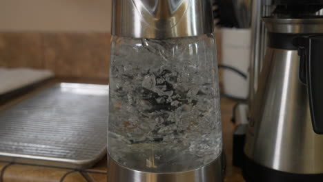 Water-boiling-and-bubbling-in-clear-glass-kettle-by-coffeemaker