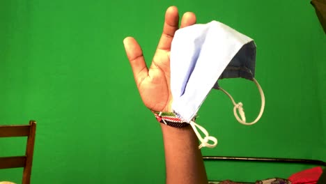 Male-arm-with-kenyan-bracelet-holding-protective-mask-in-front-of-green-screen-in-background