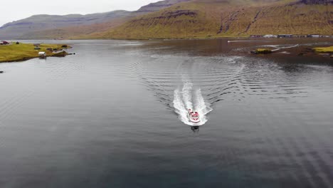 Antenne-Des-Bootes,-Das-Im-Dunklen-Wasser-In-Einem-Fjord-Segelt,-Umgeben-Von-Einer-Wunderschönen-Berglandschaft-Auf-Den-Färöer-Inseln