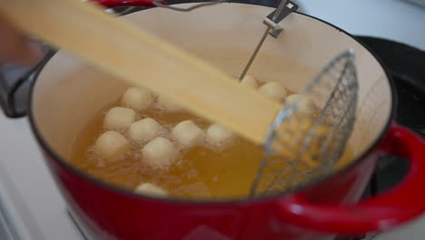 Moving-doughnut-holes-deep-frying-in-oil-with-wire-strainer,-Slow-Motion