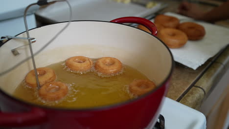 Mini-donuts-frying-in-oil-with-larger-donuts-cooling-in-background,-Slowmo