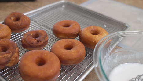 Hands-putting-fresh-homemade-donuts-on-wire-cooling-rack,-Slow-Motion