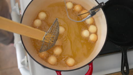 Stirring-donut-holes-frying-in-hot-oil-with-spider-strainer,-Slowmo-Overhead
