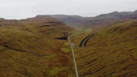 Aerial-of-long-road-in-the-nordic-landscape-of-mountains-and-grass-on-a-cloudy-day-on-the-Faroe-Islands