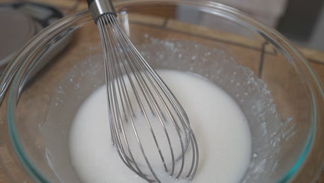 Whisk-sits-in-glass-bowl-of-white-icing-or-sugar-glaze,-Closeup-Detail