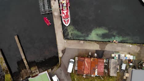 Aerial-top-down-view-of-red-and-white-boat-laying-in-dark-water-at-a-small-harbor-at-the-Faroe-Islands