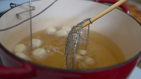 Dropping-donut-holes-dough-balls-in-deep-fry-oil-with-strainer,-Slowmo-Closeup
