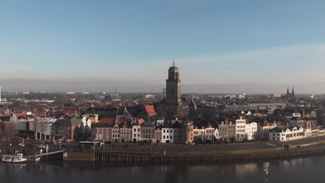 Aerial-approach-of-Dutch-Hanseatic-medieval-city-of-Deventer-in-The-Netherlands-from-the-river-IJssel-with-traffic-passing-on-the-boulevard-along-the-water-and-historic-exterior-facades