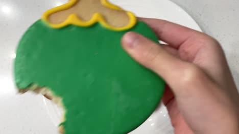 Child-taking-a-bite-out-of-a-colorfully-decorated-holiday-cookie-shaped-into-a-Christmas-ornament