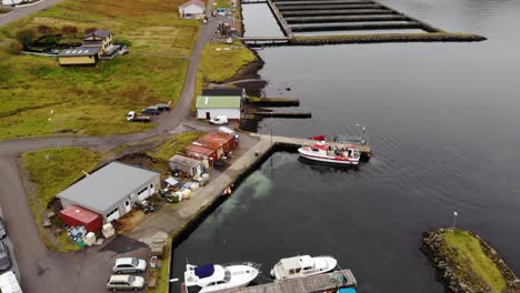 Aerial-parallax-of-of-small-harbor-with-a-red-and-white-boat-in-calm-dark-water-in-a-fjord-on-the-Faroe-Islands