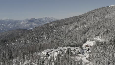 Pohorje-mountains-in-Slovenia-with-Lukov-dom-cabins-and-hotel-covered-in-snow,-Aerial-pan-left-shot