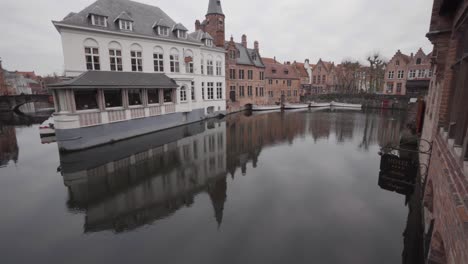 Tilt-up-shot-showing-the-canals-of-Bruges-with-historic-buildings-in-background-during-cloudy-day