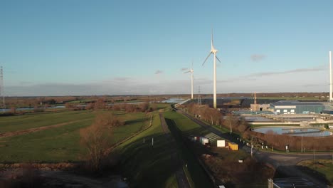 Floodplains-and-bike-path-on-a-dyke-along-industrial-area-with-wind-turbines-and-water-purification-facility-against-a-blue-sky