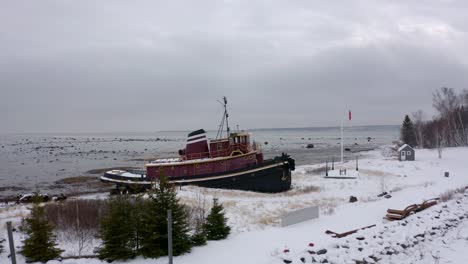 Drone-flying-over-an-old-boat-and-revealing-the-big-Saint-Lawrence-River-in-winter