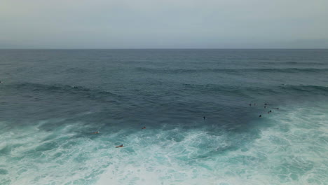 Grupo-De-Surfistas-Remando-Para-Atrapar-Olas-En-La-Vista-Aérea-Del-Océano-Pacífico-Turquesa