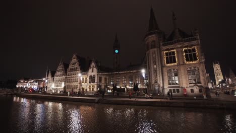 Tourist-wander-under-illuminated-gothic-buildings-along-the-Graslei,-Ghent,-Belgium