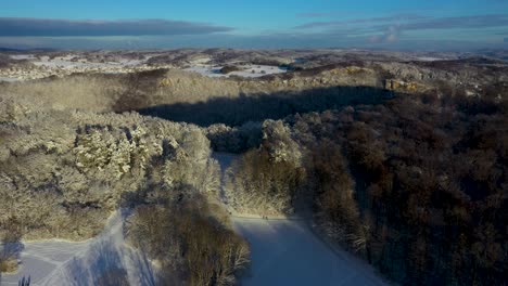 Aerial-flying-across-snow-covered-mountains-and-forest-with-blue-sky-during-winter-in-Swabia,-Germany