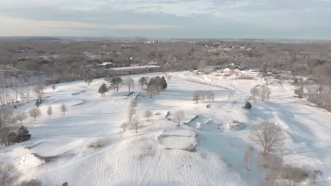 A-leftward-pan-over-a-snowy-golf-course-to-reveal-Boston,-MA,-USA-on-the-horizon