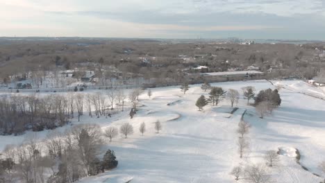 Gentle-and-slow-drone-aerial-toward-Boston-in-the-distance,-over-a-snowy-golf-course