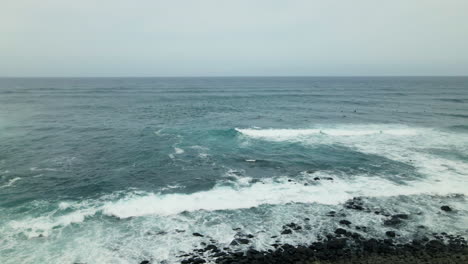 Ocean-waves-splash-on-rocky-coast-of-Maui-Island,-surfers-waiting-for-wave