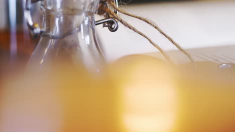 Blurry-candle-lit-in-front-of-glass-bottle-with-tag-and-band,-slider-close-up